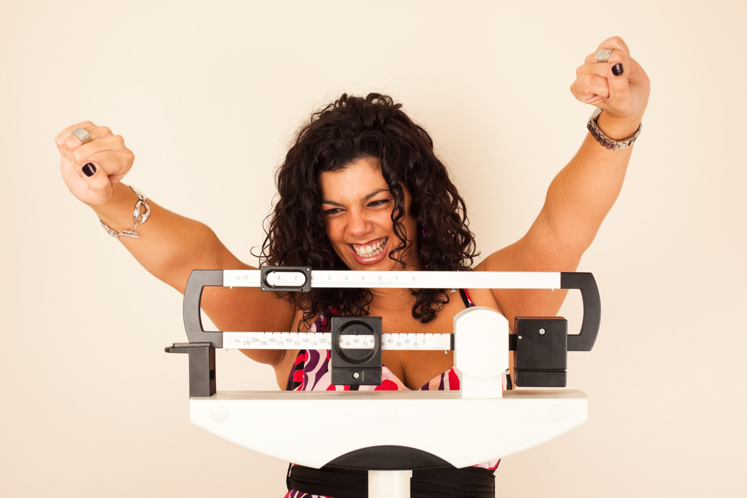 Happy woman cheering while standing on a scale after seeing results from medical weight loss treatment.